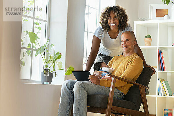 Lächelnde Familie mit digitalem Tablet und schlafendem Baby im Wohnzimmer
