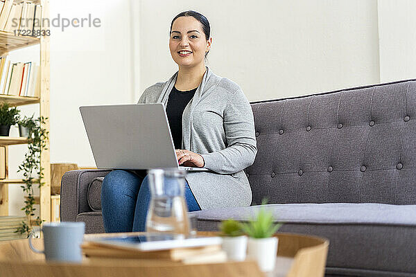 Frau  die einen Laptop benutzt  während sie zu Hause im Wohnzimmer sitzt
