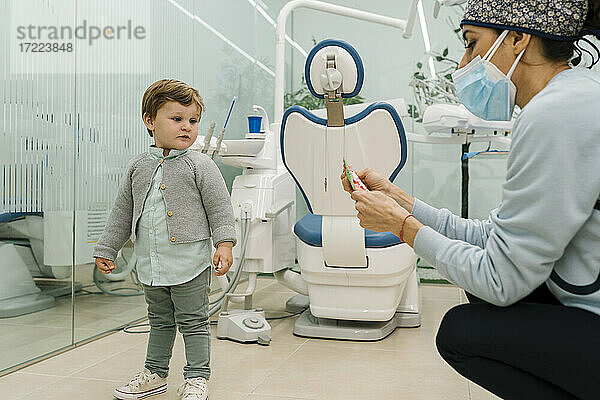 Kleiner Junge betrachtet eine Kinderzahnärztin mit Gesichtsschutzmaske in einer Klinik