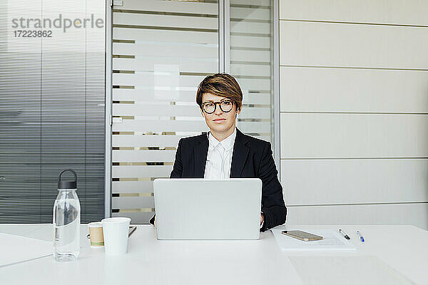 Unternehmerin schaut weg  während sie mit einem Laptop am Schreibtisch sitzt