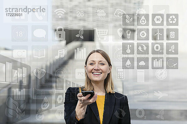 Lächelnde Geschäftsfrau  die ein Mobiltelefon mit verschiedenen Symbolen im Freien hält