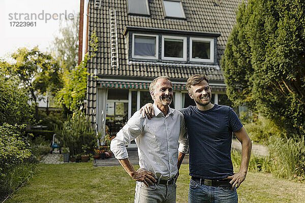 Lächelnder Sohn und Vater mit Hand auf der Hüfte im Hinterhof stehend an einem sonnigen Tag