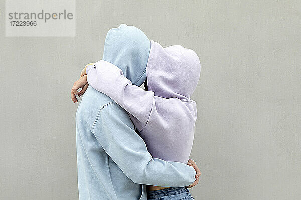 Paar in Kapuzenshirt umarmt sich gegenseitig an der Wand