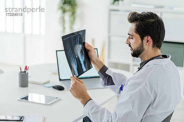 Männlicher Angestellter im Gesundheitswesen analysiert Röntgenbilder  während er am Schreibtisch im Krankenhaus sitzt