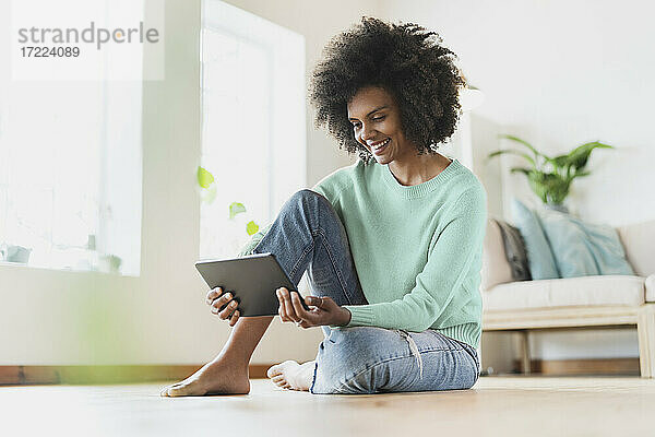Junge Frau lächelt  während sie ein digitales Tablet zu Hause benutzt