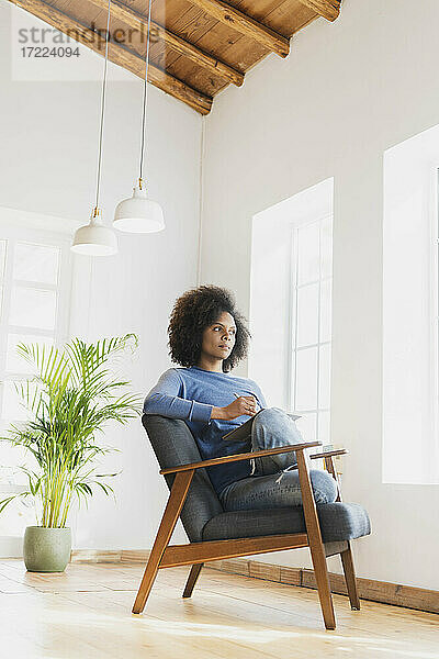 Frau schaut weg  während sie mit einem Buch auf einem Stuhl zu Hause sitzt