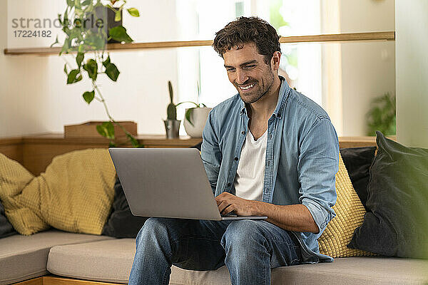 Glücklicher männlicher Freiberufler mit Laptop auf der Couch zu Hause