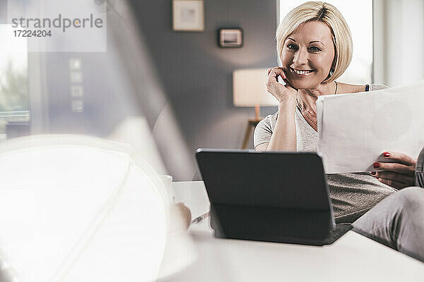 Lächelnde Frau mit digitalem Tablet und Papier zu Hause
