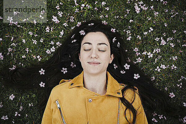 Entspannte Frau mit Blumen im Haar im Gras liegend
