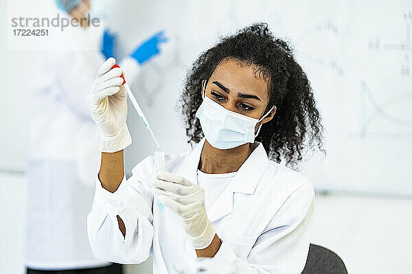 Junger Forscher beim Einfüllen von Flüssigkeit mit einer Pipette im Labor während COVID-19