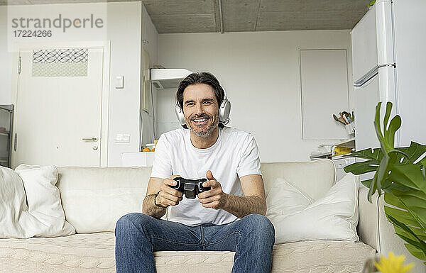 Älterer Mann mit Kopfhörern spielt ein Videospiel  während er auf dem Sofa im Wohnzimmer sitzt