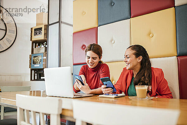 Lächelnde Frau  die das Smartphone einer Kollegin im Café benutzt