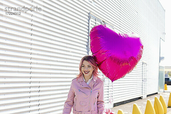 Lächelnder Mann mit glänzendem rosa Luftballon  der an einem sonnigen Tag wegschaut