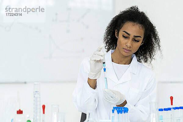 Junger Forscher  der eine Flüssigkeit in ein Reagenzglas spritzt  während er im Labor arbeitet