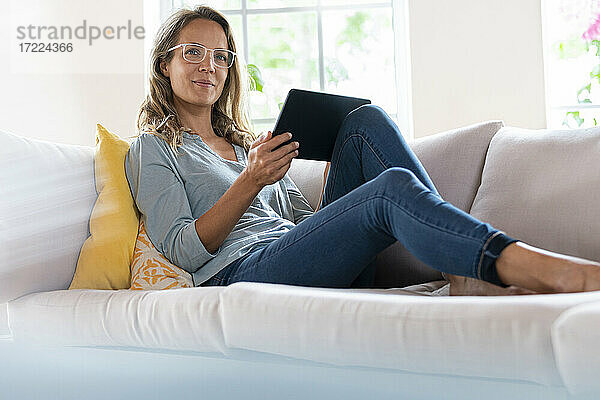 Schöne Frau mit digitalem Tablet entspannt auf Sofa im Wohnzimmer