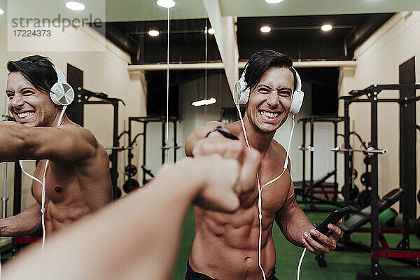 Fröhlicher Sportler mit Kopfhörern und Mobiltelefon  der einem Freund im Fitnessstudio die Faust gibt