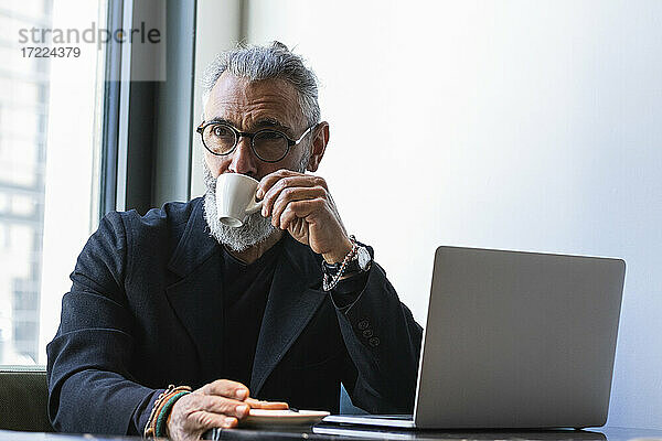 Geschäftsmann trinkt Kaffee  während er in einem Café vor einem Laptop sitzt