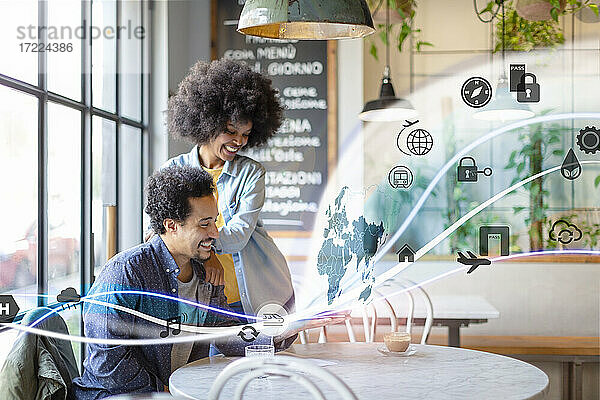 Paar schaut auf Weltkarte und Symbol aus digitalem Tablet mit leuchtendem Wellenmuster im Café