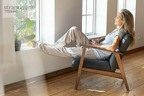 Frau mit Kaffeetasse entspannt sich auf einem Stuhl zu Hause