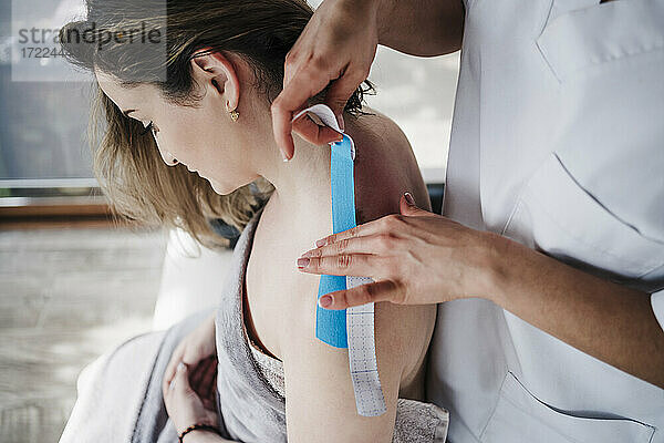 Therapeutin klebt elastisches therapeutisches Band auf die Schulter eines Patienten im Krankenhaus