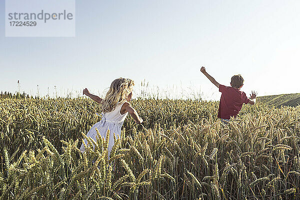 Mädchen und Junge laufen bei Sonnenuntergang durch ein landwirtschaftliches Feld