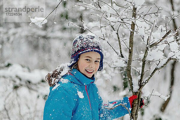 Lächelndes Mädchen schüttelt einen verschneiten Baum