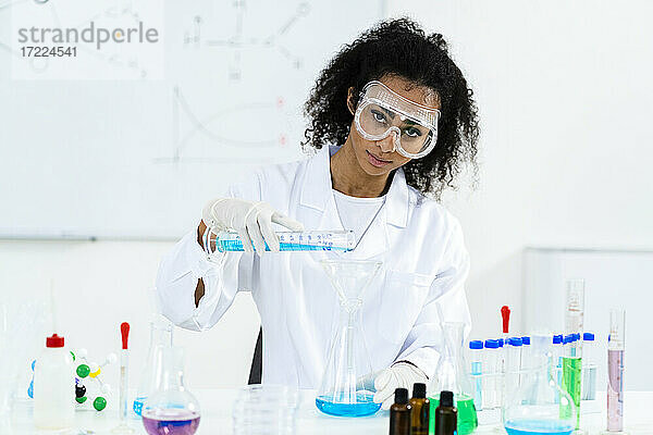 Eine Forscherin gießt eine Flüssigkeit in einen Kolben  während sie in einem Labor experimentiert