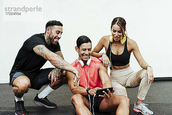 Lächelnde männliche und weibliche Athleten  die im Fitnessstudio ein Mobiltelefon benutzen