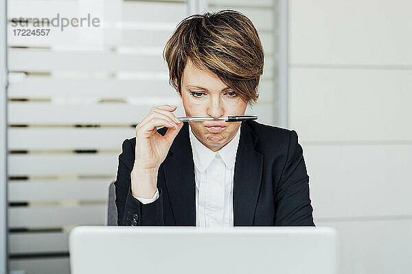Geschäftsfrau hält Stift auf den Lippen  während sie auf den Laptop im Büro schaut