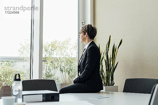 Nachdenkliche Geschäftsfrau  die wegschaut  während sie auf dem Schreibtisch im Büro sitzt