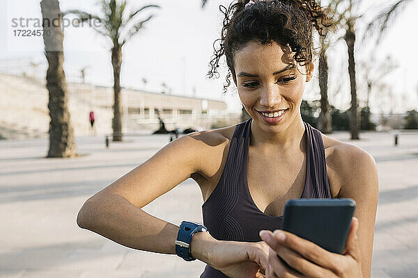 Mittlerer erwachsener Sportler  der lächelt  während er auf dem Gehweg ein Mobiltelefon benutzt