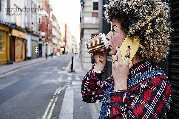 Junge Frau trinkt Kaffee  während sie mit einem Mobiltelefon spricht