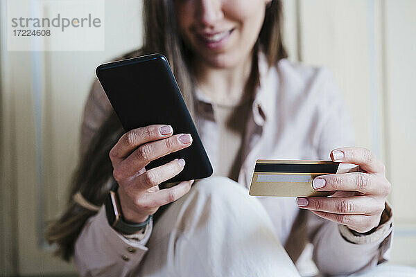 Frau  die ein Smartphone benutzt  während sie eine Kreditkarte zu Hause hält