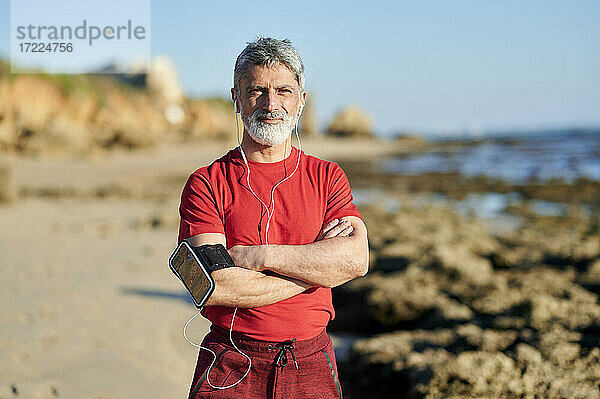 Selbstbewusster Mann mit verschränkten Armen am Strand stehend an einem sonnigen Tag