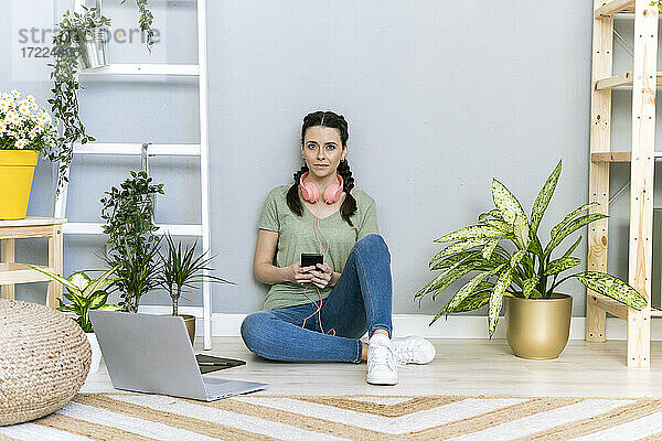 Junge Frau inmitten von Pflanzen an der Hauswand sitzend