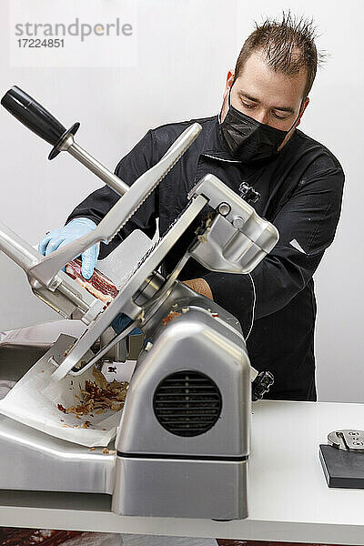 Männlicher Metzger beim Schneiden von iberischem Schinken in einer Schneidemaschine im Geschäft