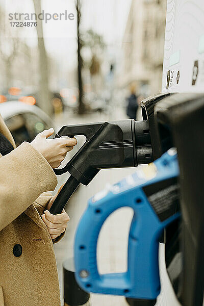 Frau hält Kabel eines Elektroautos an einer Ladestation