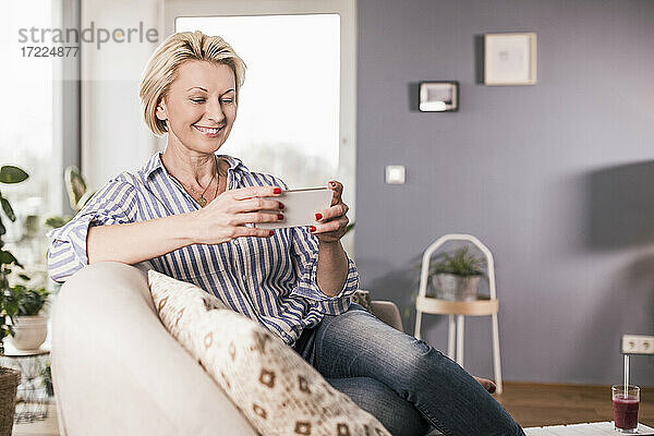 Reife Frau schaut auf Smartphone im Wohnzimmer