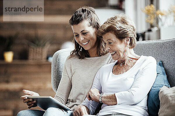 Glückliche Großmutter und Frau schauen auf ein digitales Tablet  während sie zu Hause auf dem Sofa sitzen