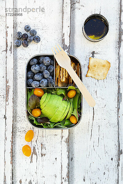 Lunchbox mit Salat  Avocado und gelben Tomaten  Crackern  Blaubeeren und Salatdressing