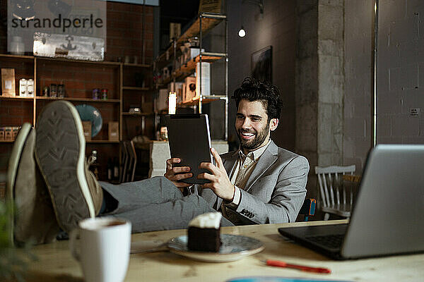 Lächelnder Geschäftsmann bei einem Videogespräch über ein digitales Tablet in einem beleuchteten Cafe