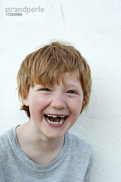 Lachender rothaariger Junge vor einer weißen Wand