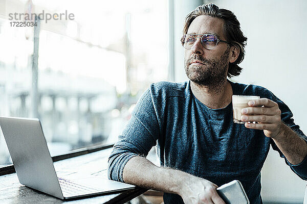 Älterer Mann mit Kaffeetasse am Laptop im Café