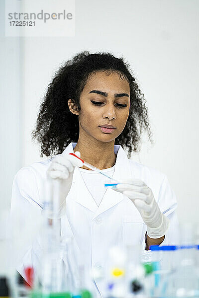 Junge Forscherin gießt Flüssigkeit mit einer Pipette in ein Labor