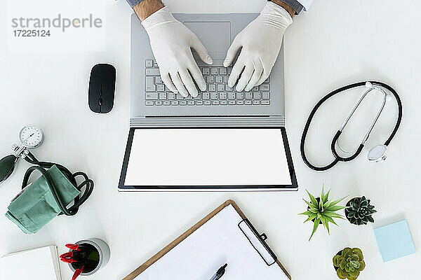 Männlicher Arzt mit chirurgischem Handschuh tippt auf einem Laptop