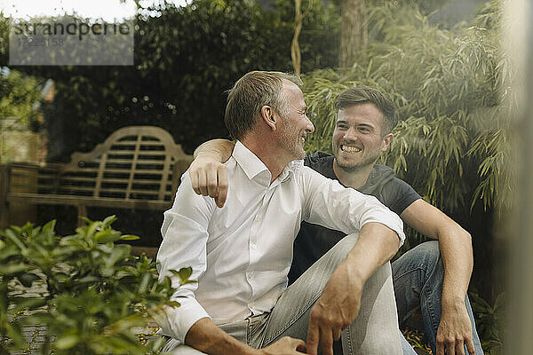Lächelnder Sohn und Vater schauen sich an  während sie im Hinterhof sitzen