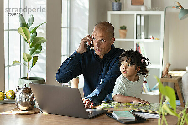 Vater telefoniert mit Handy  während er mit seiner Tochter im Home Office sitzt