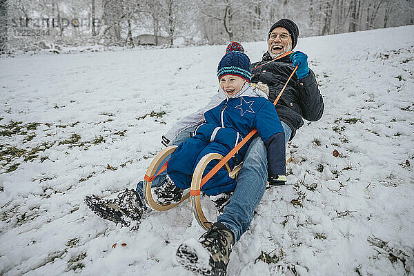 Fröhlicher Vater und Sohn beim Schlittenfahren auf einem verschneiten Hügel im Winter