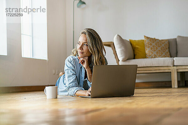 Nachdenkliche Frau  die wegschaut  während sie mit ihrem Laptop zu Hause liegt