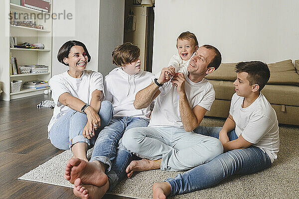 Fröhliche Familie sitzt auf dem Teppich im Wohnzimmer zu Hause
